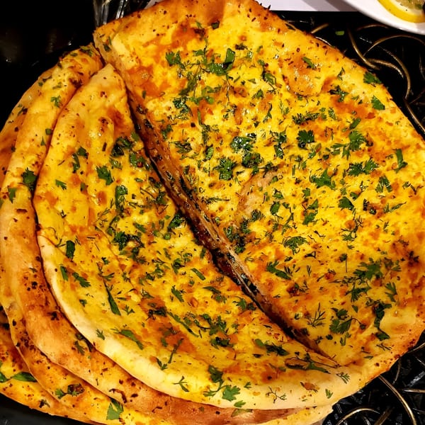 Golden garlic naan bread, garnished with fresh green herbs, stacked on a dark surface.