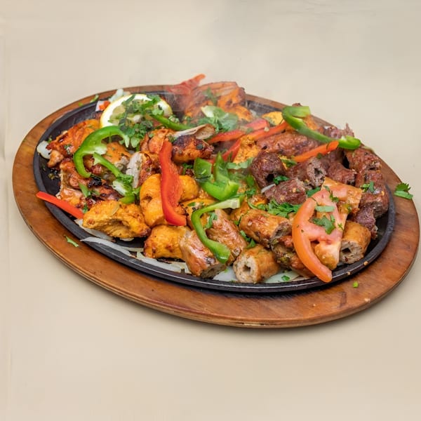Sizzling platter of Haveli Grill's mixed Pakistani BBQ, including chicken, beef, and seekh kebabs, with vegetables.