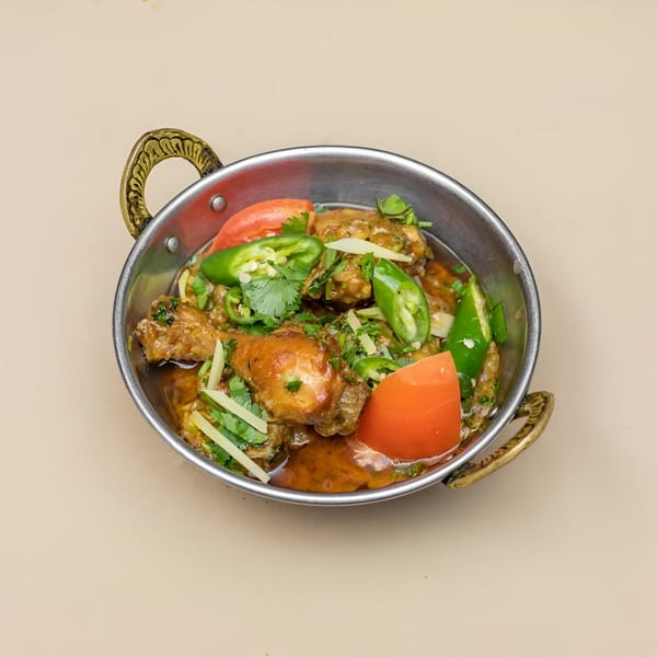 Pakistani chicken karahi with tomatoes, green chilies, and cilantro in a metal bowl.