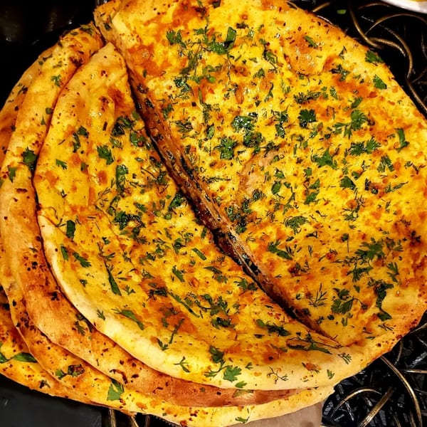 Close-up of golden Pakistani naan bread topped with fresh green herbs, stacked on a dark grill.