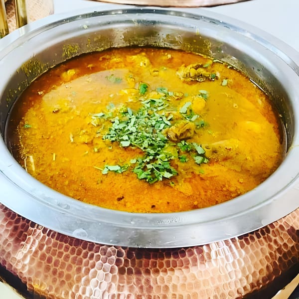 A large metal pot filled with a rich, yellow Pakistani curry, garnished with fresh green herbs.