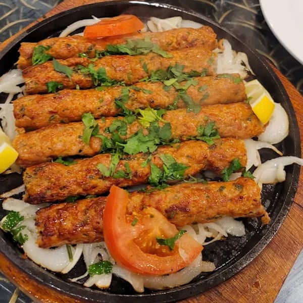 Sizzling Haveli Grill seekh kebabs with onions, tomatoes, lemon, and cilantro on a hot platter.