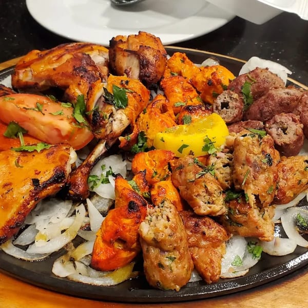 A sizzling platter of Pakistani BBQ, including chicken tikka, seekh kebabs, and grilled tomatoes and onions.