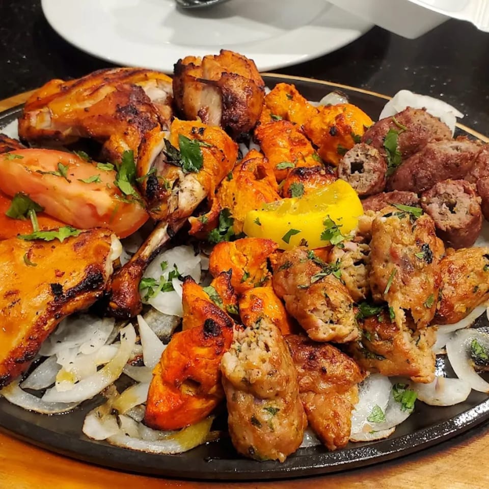 A sizzling platter of Pakistani BBQ, including chicken tikka, seekh kebabs, and grilled tomatoes and onions.