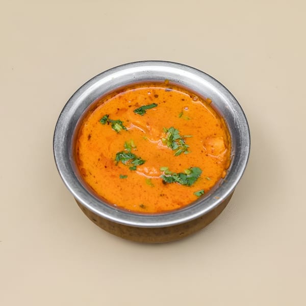 A metal bowl filled with orange Pakistani curry, garnished with fresh green cilantro, on a light background.